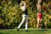 A couple playing golf together, with the man teeing off and the woman observing in a relaxed setting.